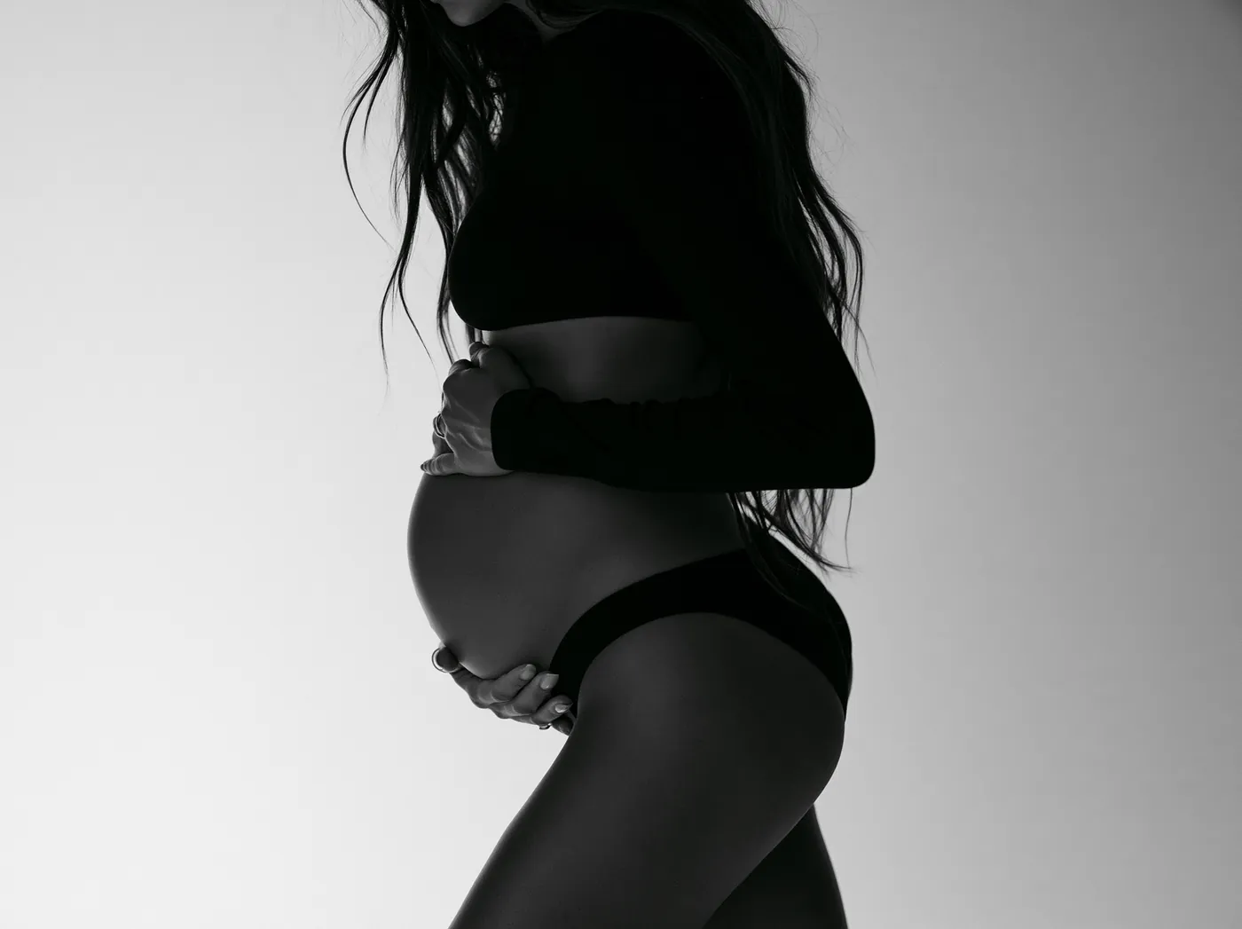 Black and white maternity profile portrait, hands beneath the belly
