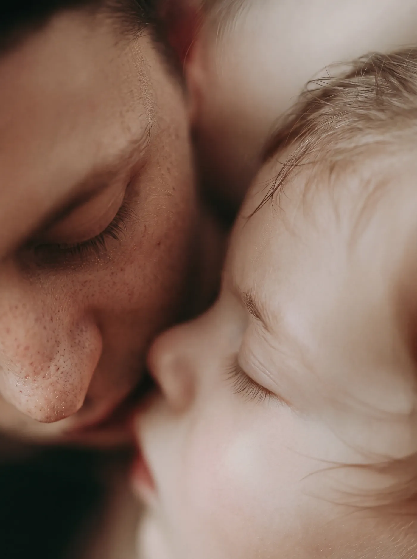 Parent's face resting against a sleeping six week old newborn